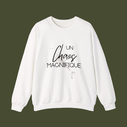 A white crewneck sweatshirt featuring a black graphic print on the front that reads 'UN Chaos MAGNIFIQUE' with a small illustration of a wand, displayed against a clean white background.