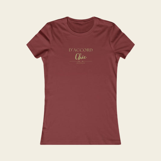 A women's short-sleeve crewneck t-shirt in a muted brick red color, featuring the text 'D'ACCORD Chic' printed in a gold metallic-style font on the chest, displayed against background.
