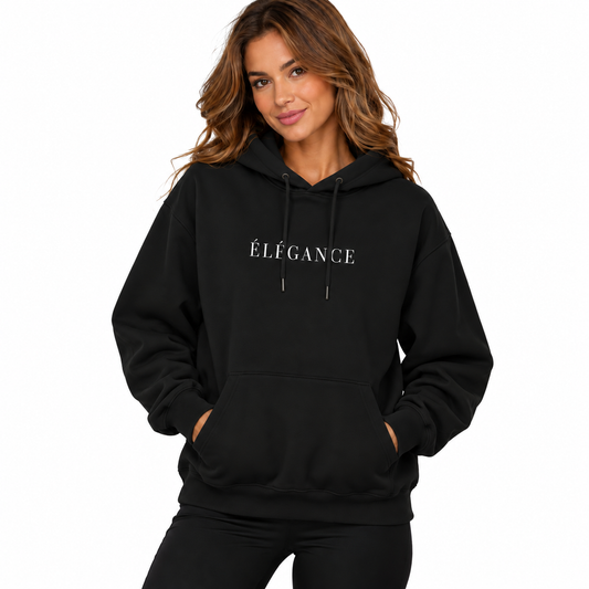 A woman wearing a black pullover hoodie with the word 'ÉLÉGANCE' printed in white serif letters across the chest, posed against a solid white background.