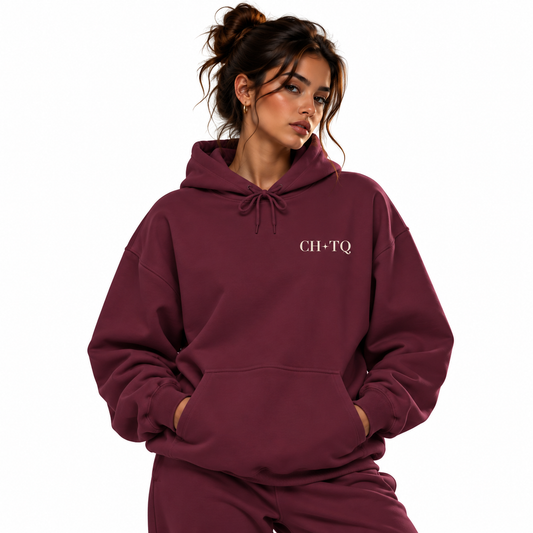 A woman wearing a matching burgundy sweatshirt and pants set, featuring the text 'CH-TQ' printed in white on the left chest, set against a plain white background.