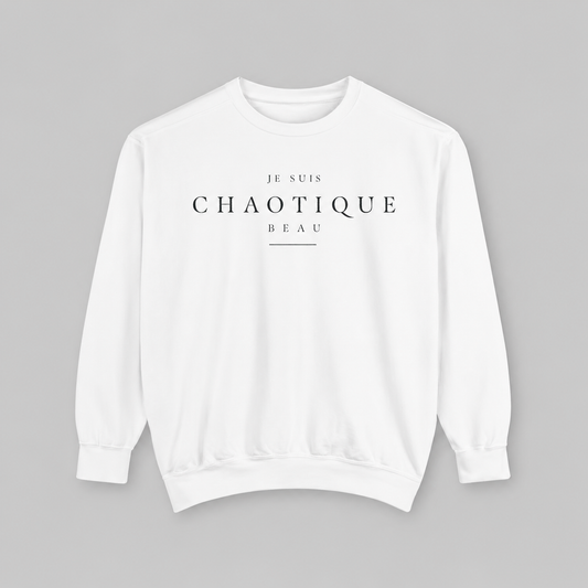 A white crewneck sweatshirt with black printed text reading 'JE SUIS CHAOTIQUE BEAU' on the chest, displayed flat against a solid gray background.