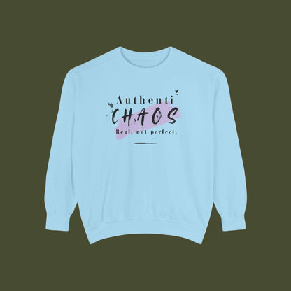 A light blue crewneck sweatshirt with a graphic on the chest that reads 'Authenti CHAOS Real, not perfect.' in black and dark purple lettering over a pink paint splatter background.
