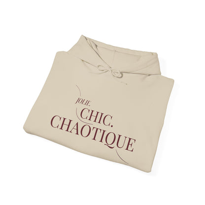 A folded beige hoodie with a graphic of a fishing rod and the text 'Jolie. Chic. Chaotique' printed on the front, shown on a plain white background.
