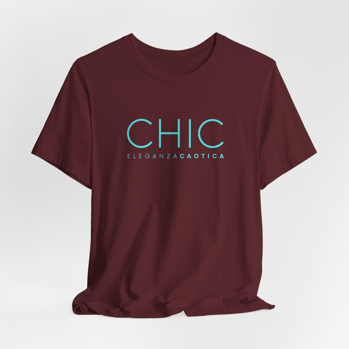 Maroon graphic T-shirt with pink 'CHIC ELEGANZA CAOTICA' typography on a neutral gray studio background.