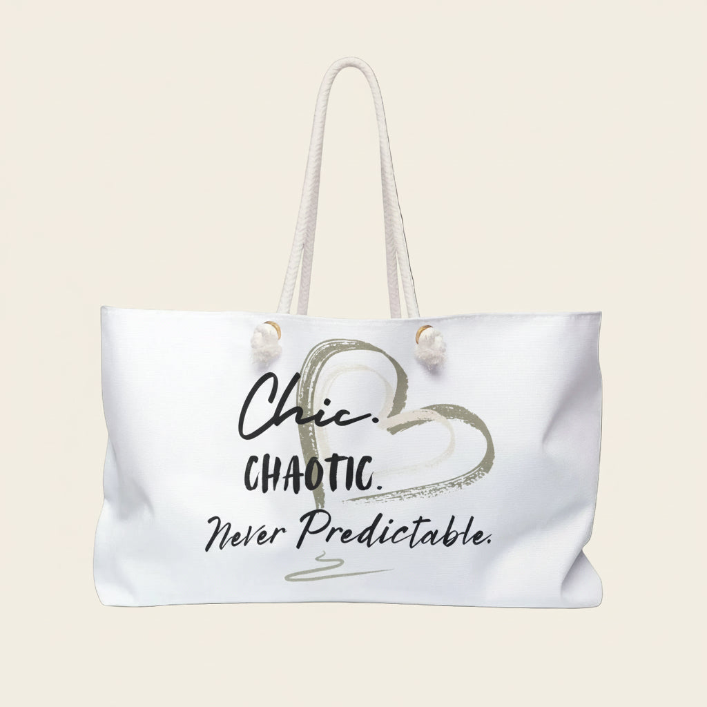 A white tote bag with cream rope handles, featuring a graphic print of a heart and the text 'Chic. CHAOTIC. Never predictable'