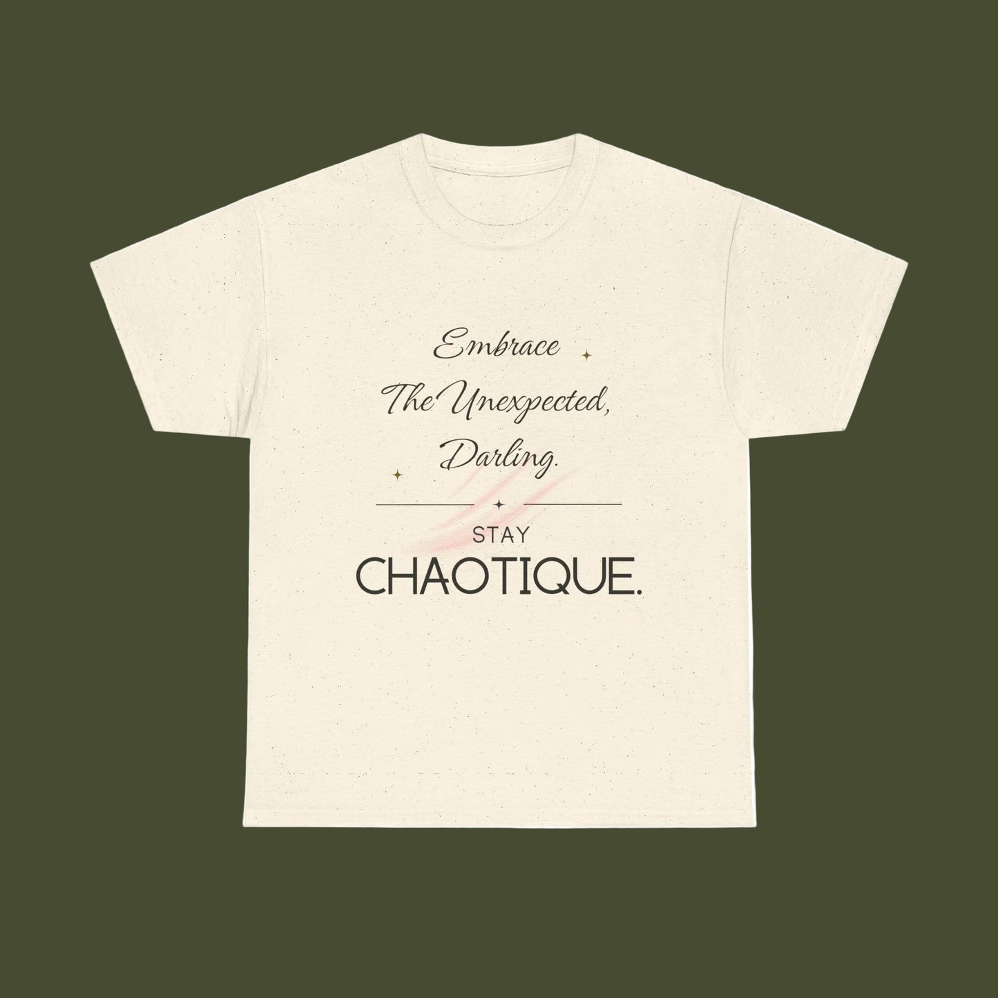 An off-white short-sleeve t-shirt with a printed graphic on the front. The graphic features the text 'Embrace The Unexpected, Darling' in a cursive font, a thin horizontal line, 'STAY' in a block font, and 'CHAOTIQUE.