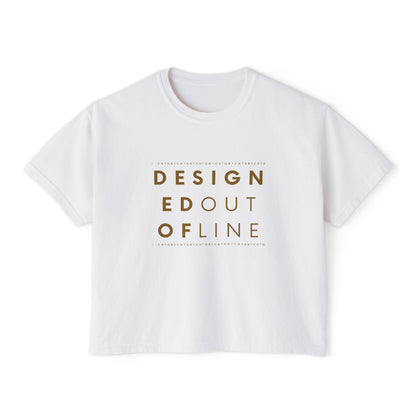 A white short-sleeve boxy T-shirt with a slightly cropped fit and a gold typography graphic on the front reading “DESIGNED OUT OF LINE.”