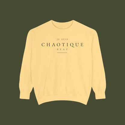 A pale yellow crewneck sweatshirt with 'JE SUIS CHAOTIQUE BEAU' printed in black serif text on the chest, displayed flat against a solid white background.