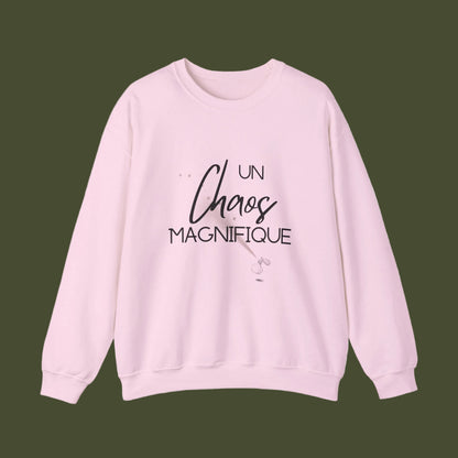 A light pink crewneck sweatshirt featuring the French phrase 'UN Chaos MAGNIFIQUE' printed in black across the chest, displayed on a clean white background.