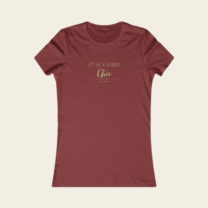A women's short-sleeve crewneck t-shirt in a muted brick red color, featuring the text 'D'ACCORD Chic' printed in a gold metallic-style font on the chest, displayed against background.
