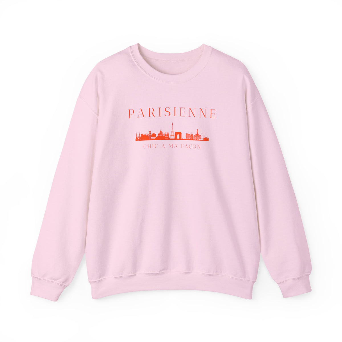 A light pink crewneck sweatshirt with a bright orange “PARISIENNE” graphic, Paris skyline design, and “CHIC À MA FAÇON” text on the chest, displayed against a clean white background.