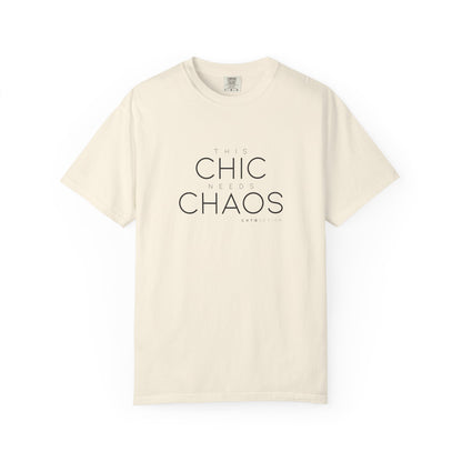 An light beige crewneck t-shirt with the text 'THIS CHIC NEEDS CHAOS' printed in black on the front, displayed on a clean white background.