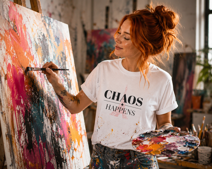 Artist painting on an easel wearing a white t-shirt with 'CHAOS HAPPENS' text.