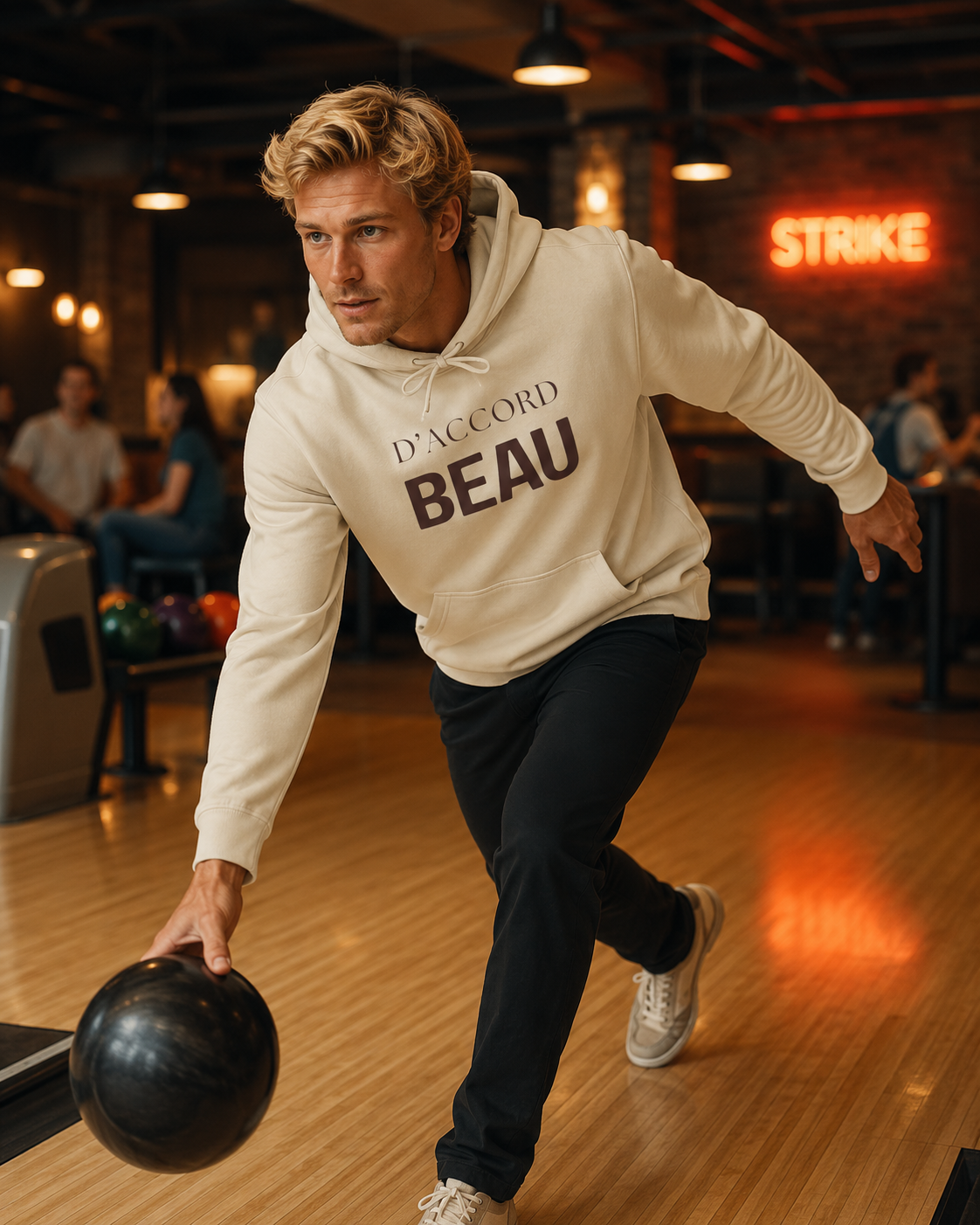 A man bowling in a bowling alley wearing a cream-colored hoodie with 'D'ACCORD BEAU' printed on the front, paired with dark pants and white sneakers.