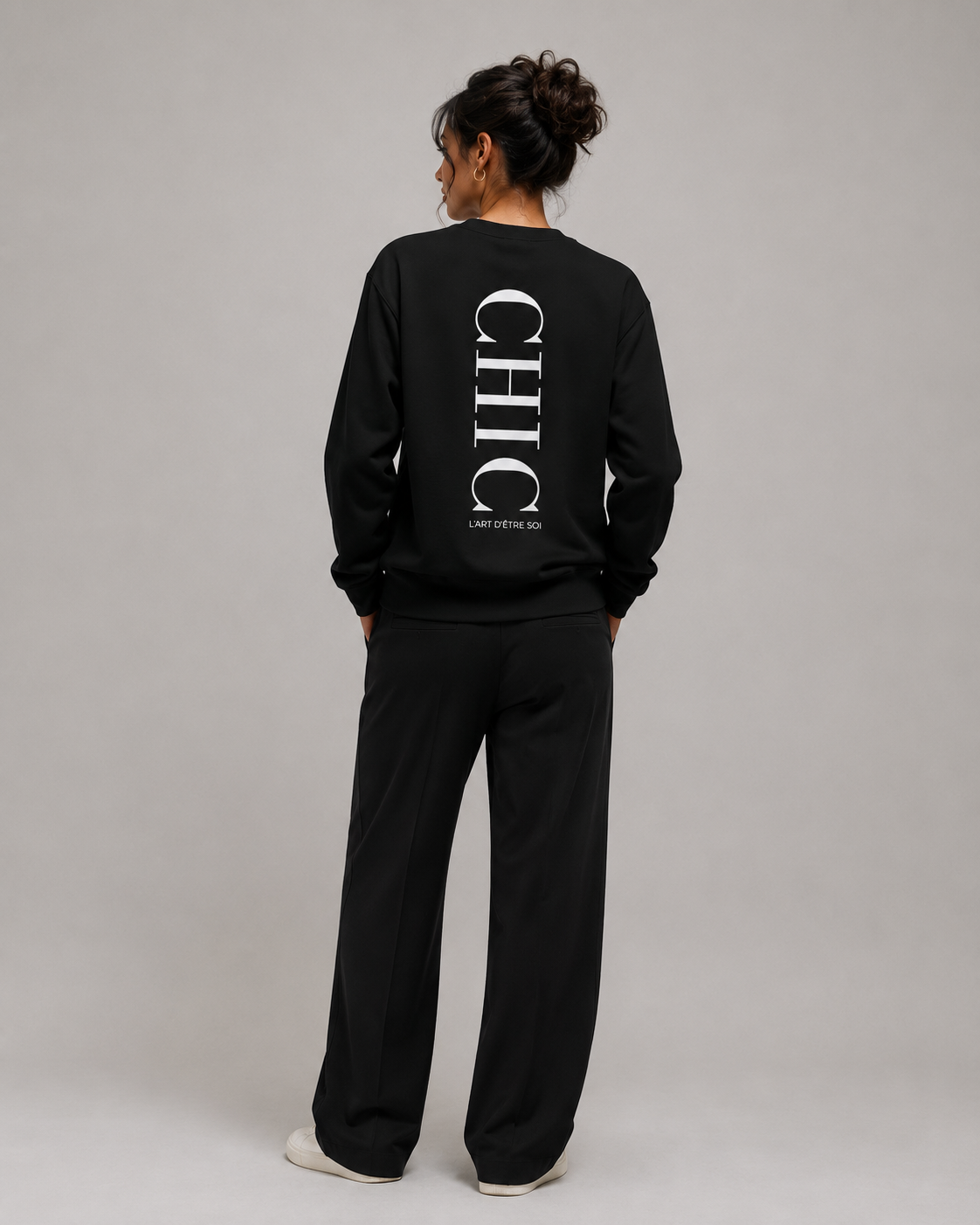 A model shown from the back wearing a black sweatshirt and matching sweatpants set. The sweatshirt features a large vertical white 'CHIC' logo on the back with smaller text underneath.