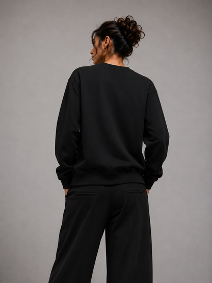 A person shown from the back wearing a black crewneck sweatshirt and black wide-leg pants against a plain gray studio background.