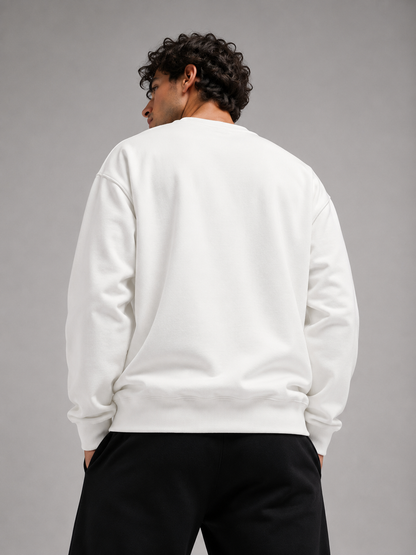 A man viewed from behind wearing a plain white crewneck sweatshirt and black pants, standing against a solid gray studio background.