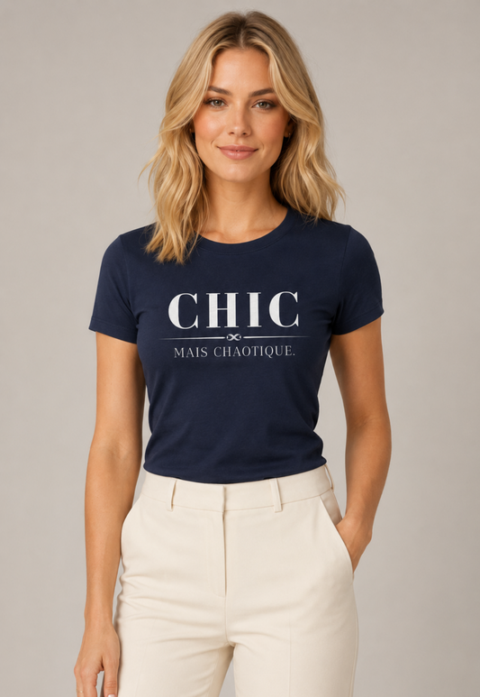 Young woman wearing a navy CHIC MAIS CHAOTIQUE graphic T-shirt with minimalist white French-inspired typography, styled with cream trousers in a modern light gray studio setting.