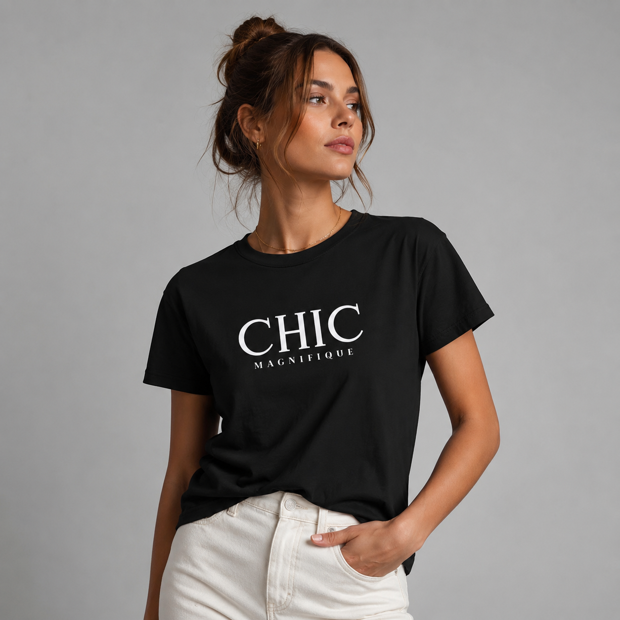 Woman wearing a black CHIC MAGNIFIQUE graphic T-shirt with white French-inspired typography, paired with off-white trousers in a neutral gray studio setting.