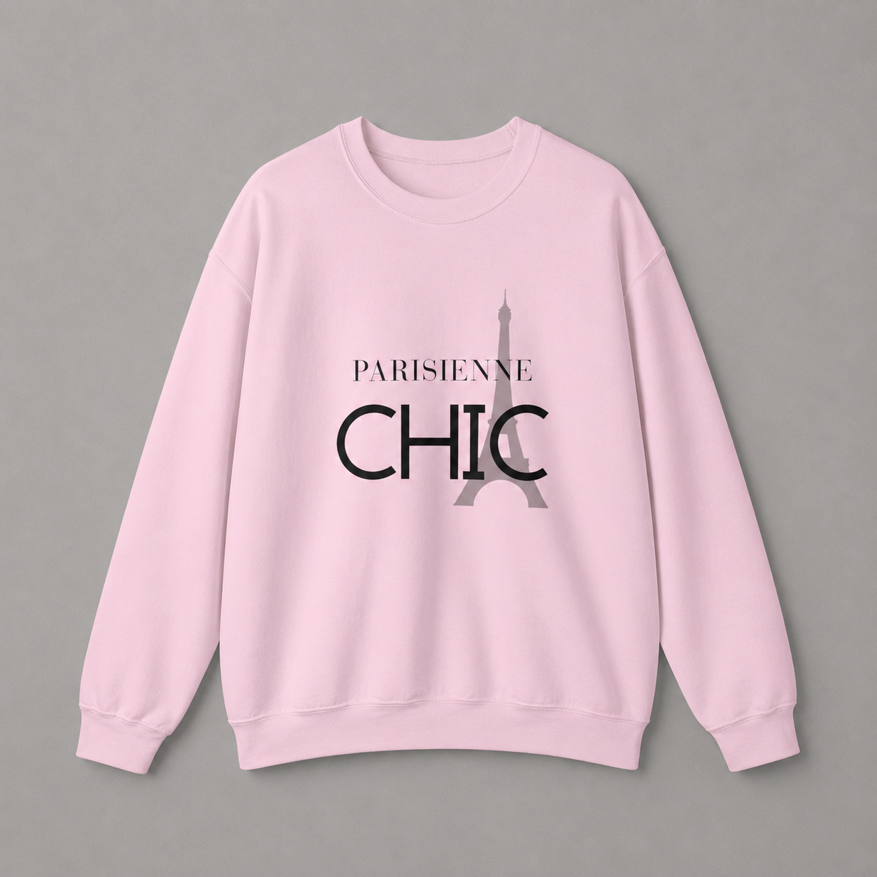Light pink crewneck sweatshirt featuring a “PARISIENNE CHIC” graphic with a stylized Eiffel Tower, displayed against a neutral gray studio background.