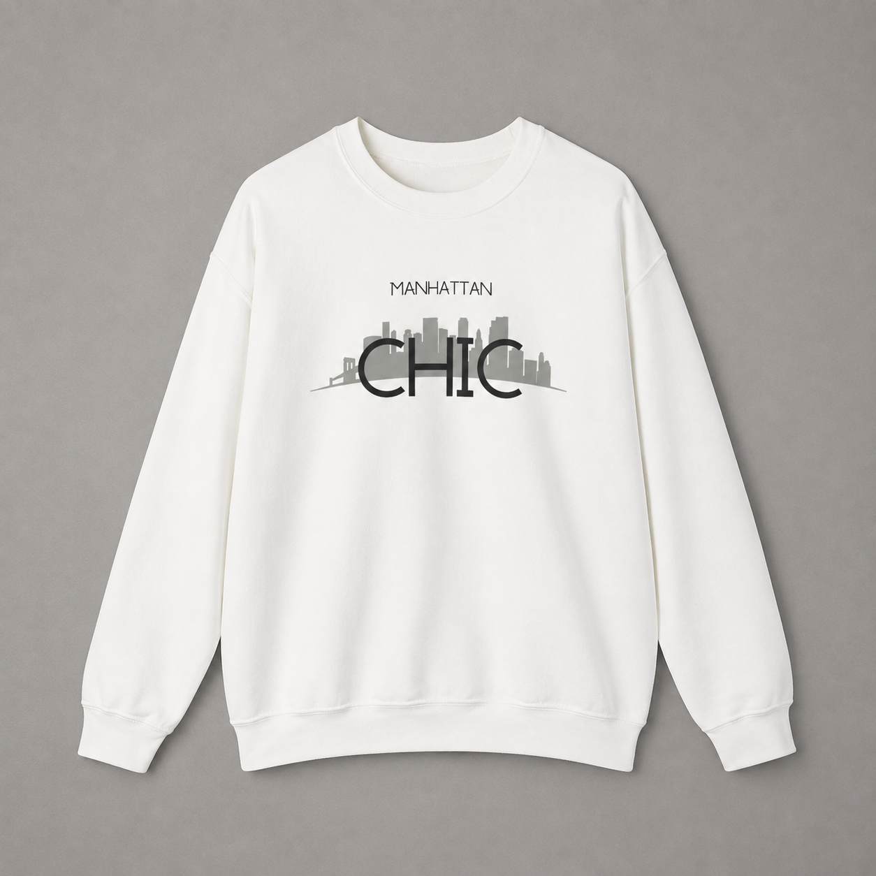 White MANHATTAN CHIC crewneck sweatshirt featuring black typography and a muted olive New York skyline graphic, 
 against a neutral gray studio background.