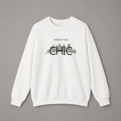 White MANHATTAN CHIC crewneck sweatshirt featuring black typography and a muted olive New York skyline graphic, 
 against a neutral gray studio background.