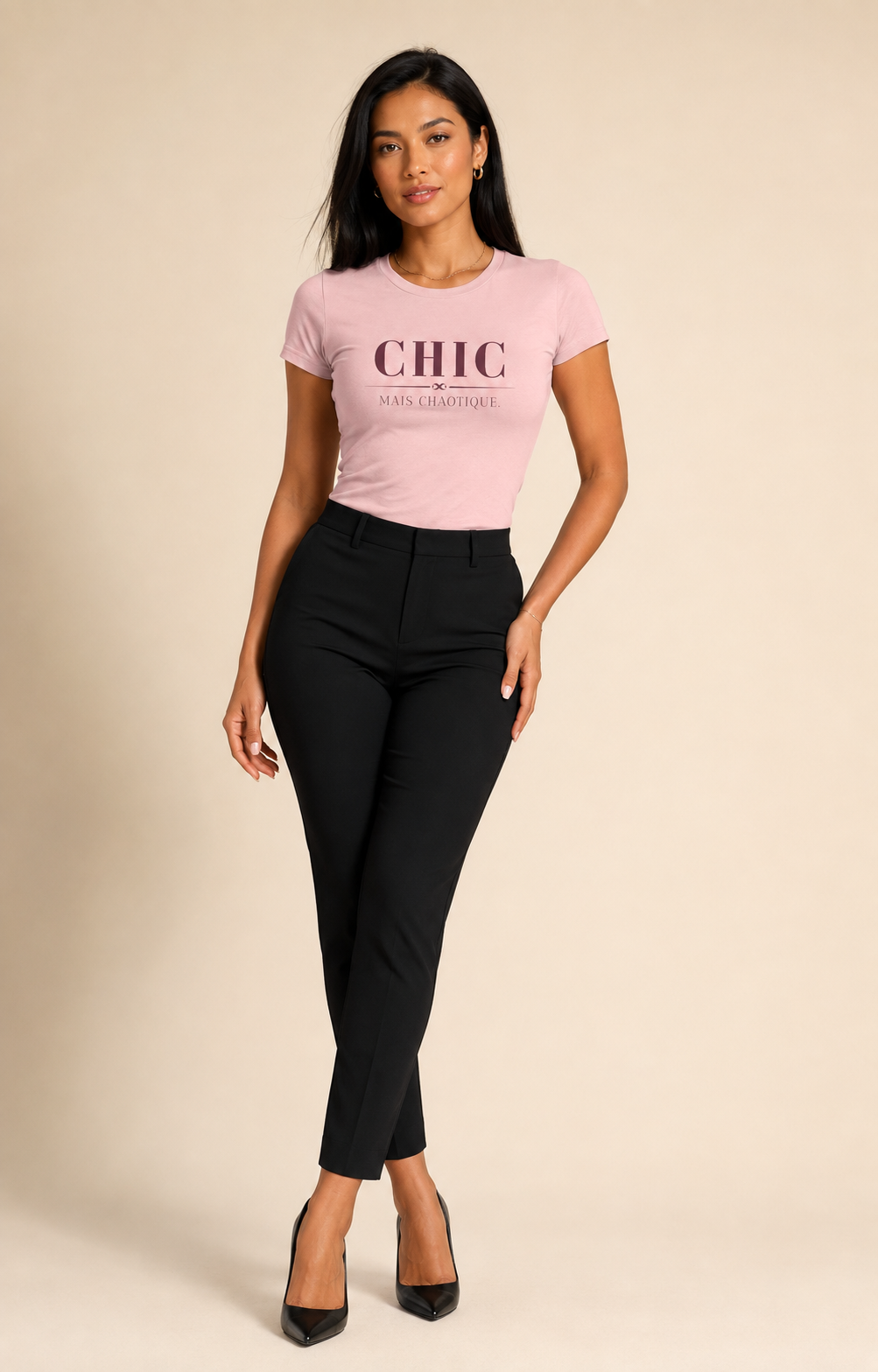 A woman modeling a light pink short-sleeve t-shirt with 'CHIC' printed on the chest, paired with black cropped pants and black heels, against a solid beige background.