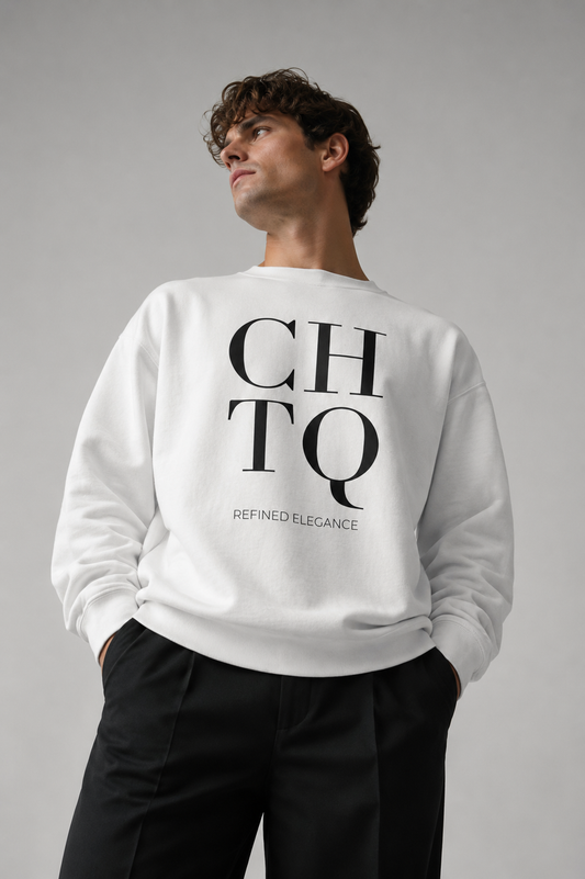 Man wearing a white CHTQ Refined Elegance crewneck sweatshirt with a large black logo on the back, styled with black trousers against a neutral gray studio background.