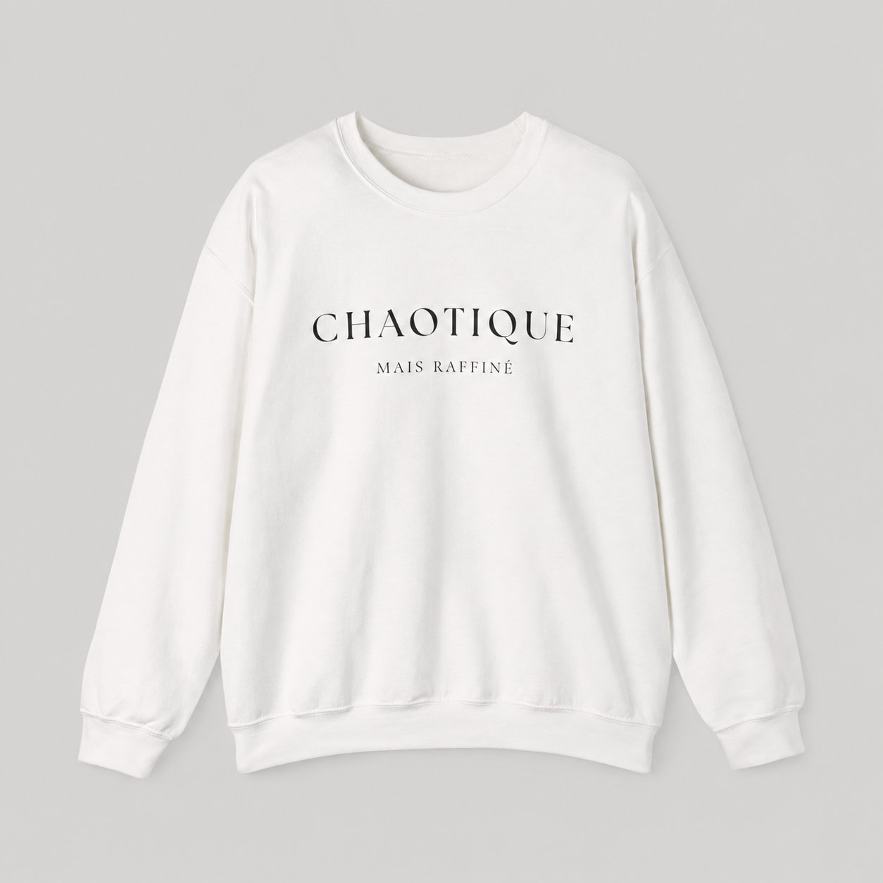 White sweatshirt on a white background featuring a “Chaotique Mais Raffiné” graphic text print.