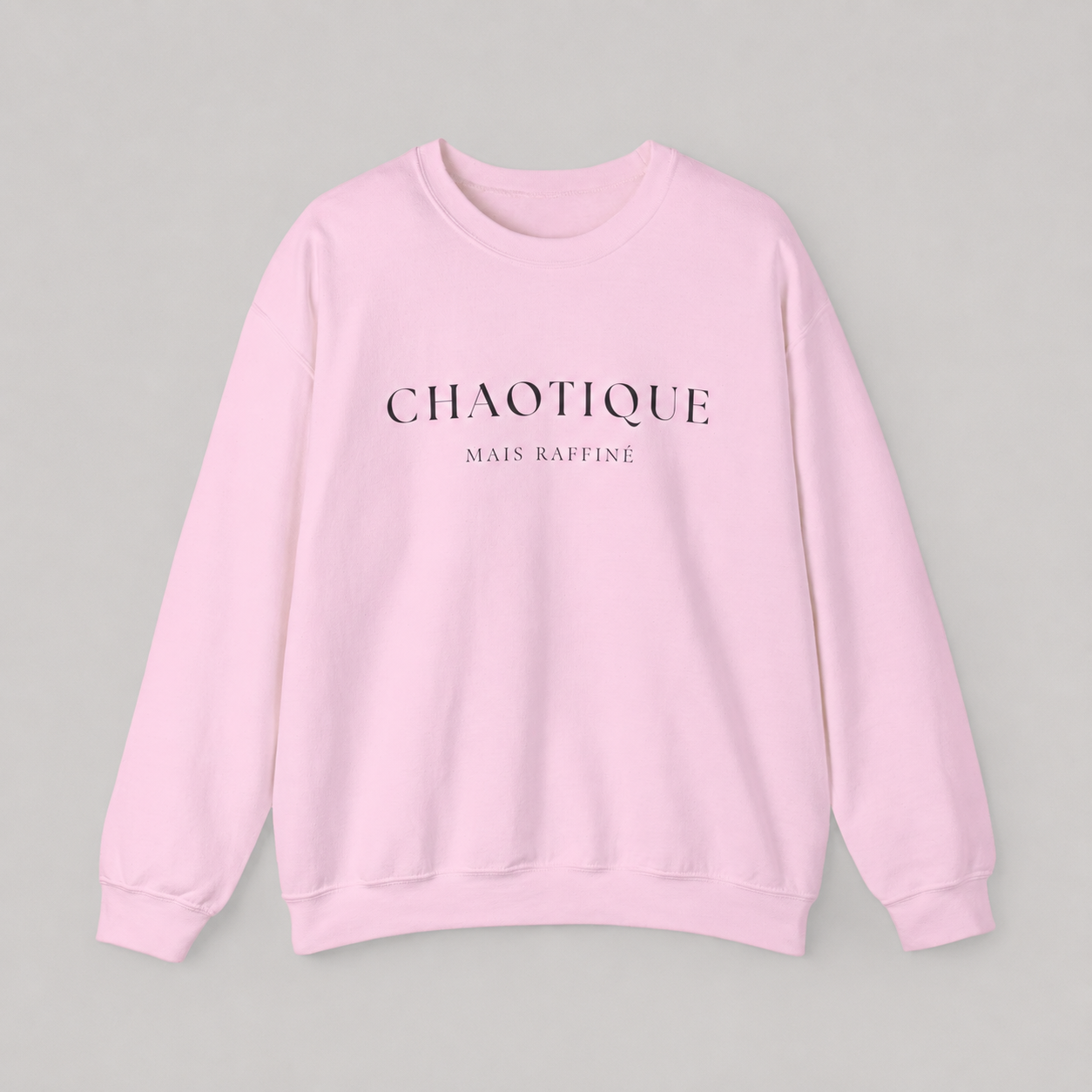 Light pink sweatshirt on a white background featuring a “Chaotique Mais Raffiné” graphic text print.