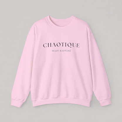 Light pink sweatshirt on a white background featuring a “Chaotique Mais Raffiné” graphic text print.
