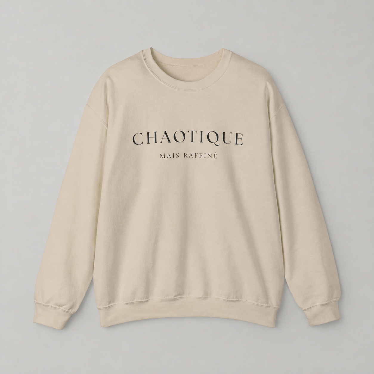 Cream color sweatshirt on a white background featuring a “Chaotique Mais Raffiné” graphic text print.