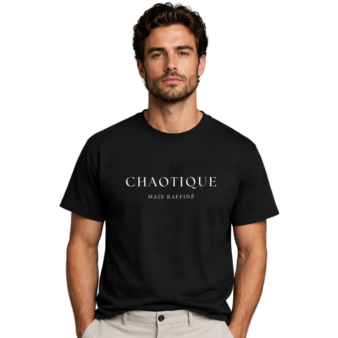A man wearing a black short-sleeve crewneck t-shirt with 'CHAOTIQUE MAIS RAFFINE' printed in white across the chest, paired with light beige trousers, against a solid gray studio background.