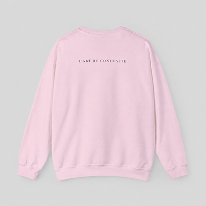 A light pink crewneck sweatshirt shown from the back, featuring the text 'L'ART DU CONTRASTE' printed in small black capital letters across the upper back, set against a solid light gray background.