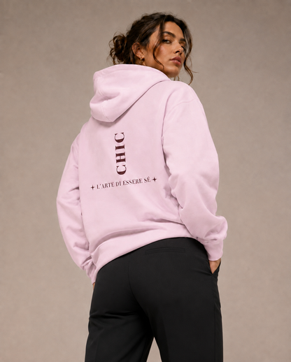 A woman wearing a light pink graphic hoodie with dark pink back print, photographed from behind in a minimalist beige studio setting.