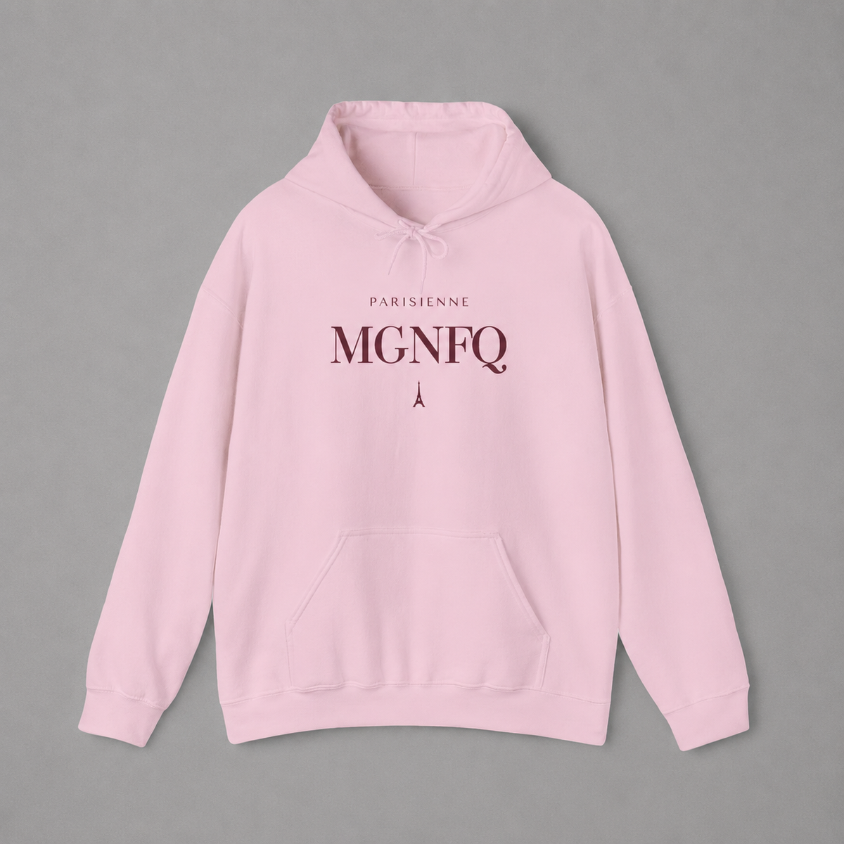 Light pink PARISIENNE MGNFQ graphic hoodie featuring cream typography and a small Eiffel Tower detail, shown against a light gray studio background.