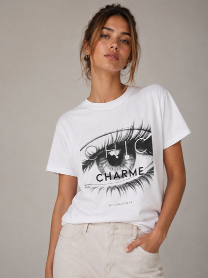 Woman wearing a white CHIC CHARME graphic T-shirt featuring a bold black-and-white eye print, styled with neutral trousers in a minimalist studio setting.