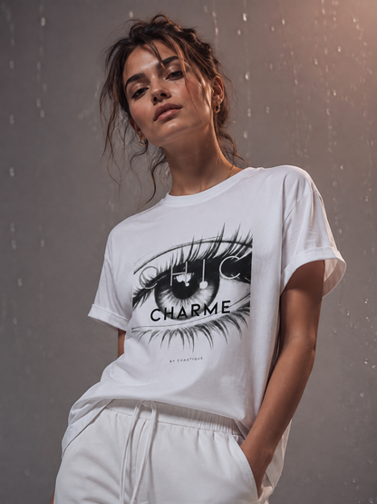 Woman wearing a white CHIC CHARME graphic T-shirt with a monochrome eye print, styled in a gray editorial studio with subtle rose-gold lighting.