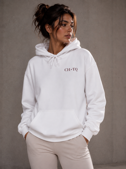A woman wearing a white CH*TQ graphic hoodie with dark red typography, photographed in a neutral gray studio background.