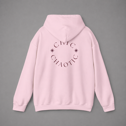 Light pink pullover hoodie shown from the back, featuring a dark burgundy circular CHIC CHAOTIC graphic with subtle star accents against a neutral gray studio background.