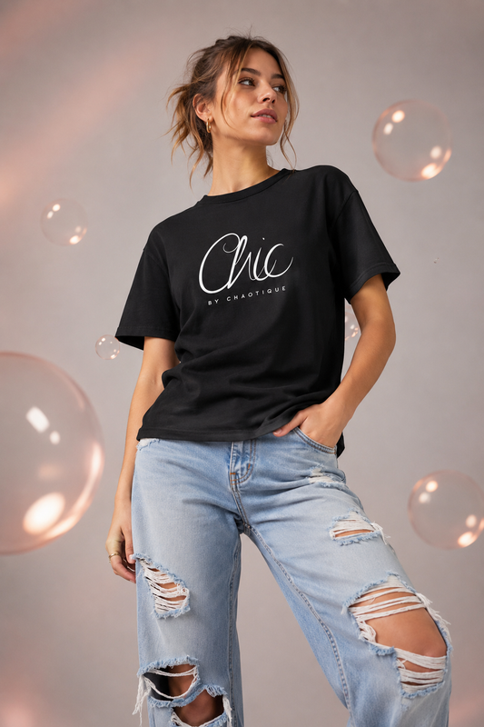 Woman wearing a black Chic by Chaotique graphic T-shirt with light blue ripped jeans in a modern studio setting.