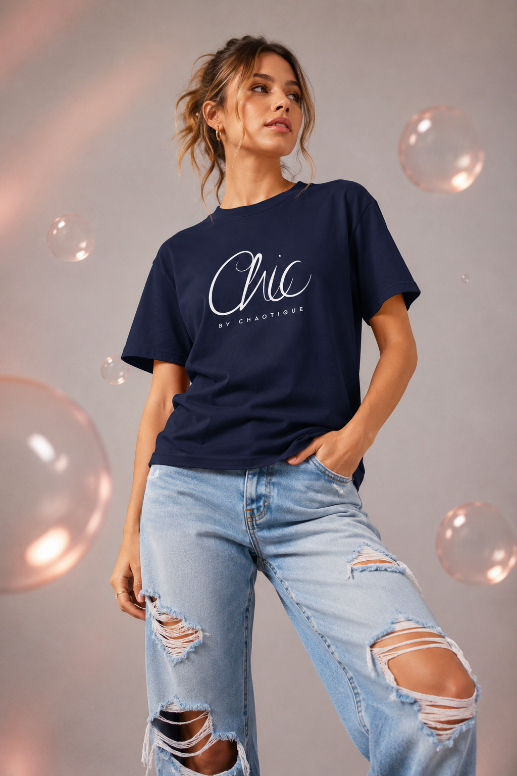 Woman wearing a navy blue Chic by Chaotique graphic T-shirt with light blue ripped jeans in a modern studio setting.