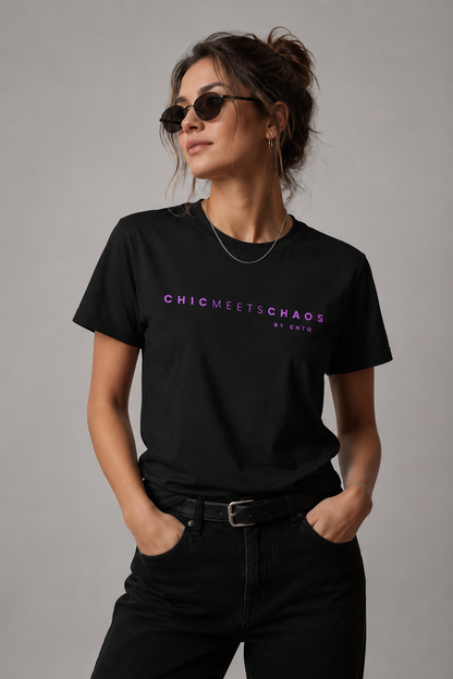 Woman wearing a black Chic Meets Chaos by CHTQ graphic T-shirt with purple typography, paired with black jeans against a gray studio background.