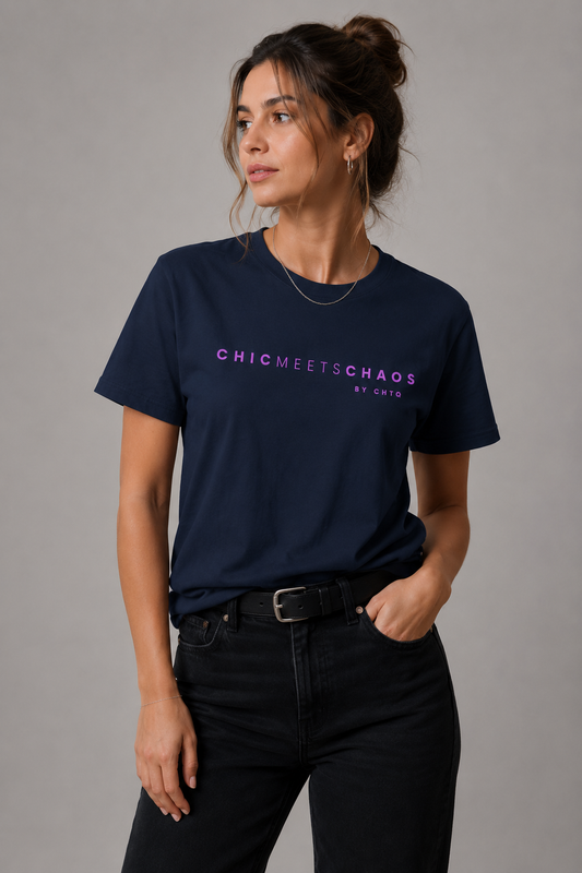 Woman wearing a navy blue Chic Meets Chaos by CHTQ graphic T-shirt with purple typography, paired with black jeans against a gray studio background.