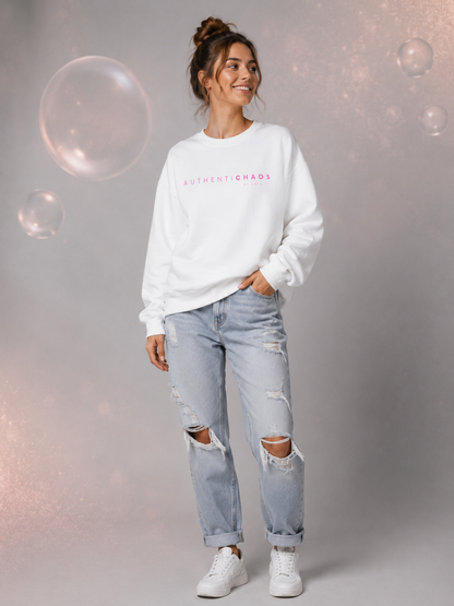 Woman wearing a white AuthentiCHAOS graphic sweatshirt with pink lettering in a modern gray studio setting.