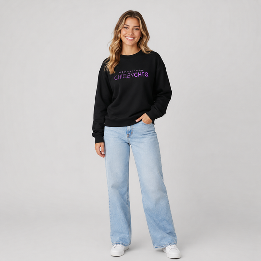 A woman modeling a black crewneck sweatshirt with purple text reading “CHIC BY CHTQ” and “REBELLE DANS L’ÂME” above it, paired with light blue jeans and white sneakers against a light gray studio background.