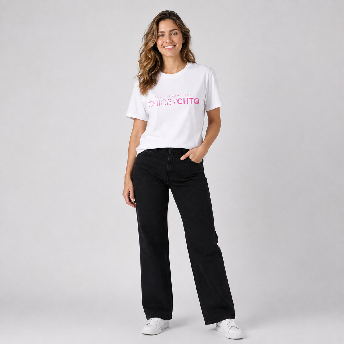 A woman modeling a white short-sleeve graphic T-shirt featuring pink and white “CHIC BY CHTQ” text with “REBELLE DANS L’ÂME” above, paired with black jeans and white sneakers against a cool light gray studio background.