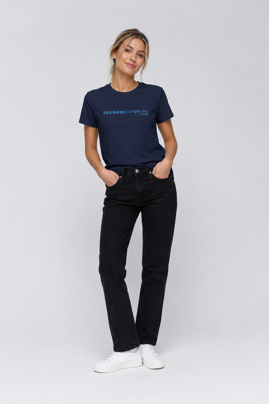 A woman modeling a navy blue crewneck T-shirt with light blue text that reads “DESIGNED OUT OF LINE” and “BY CHTQ” on the chest, paired with black jeans and white sneakers, against a light gray studio background.