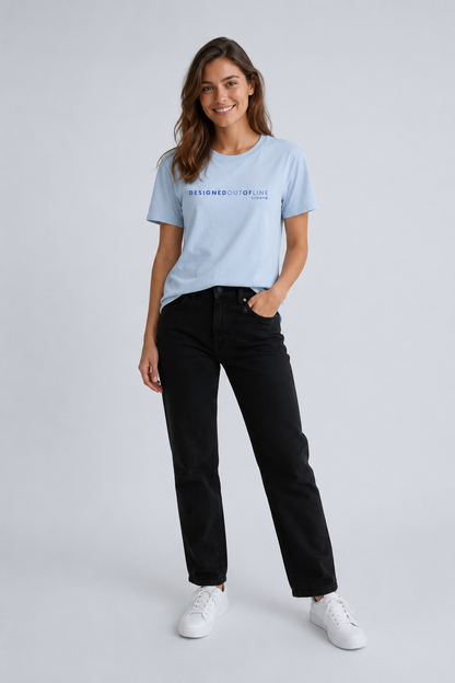 A woman modeling a light blue crewneck T-shirt with blue text that reads “DESIGNED OUT OF LINE” and “BY CHTQ” across the chest, paired with black jeans and white sneakers, against a light gray studio background.