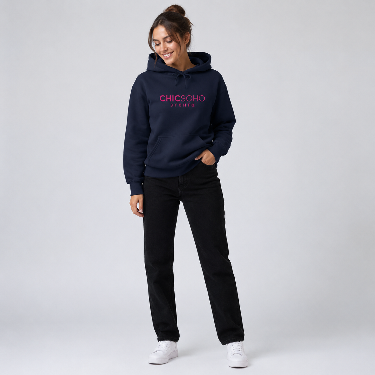 A woman modeling a navy blue pullover hoodie with “CHICSOHO BY CHTQ” printed in pink across the chest, paired with black pants and white sneakers, against a light gray studio background.